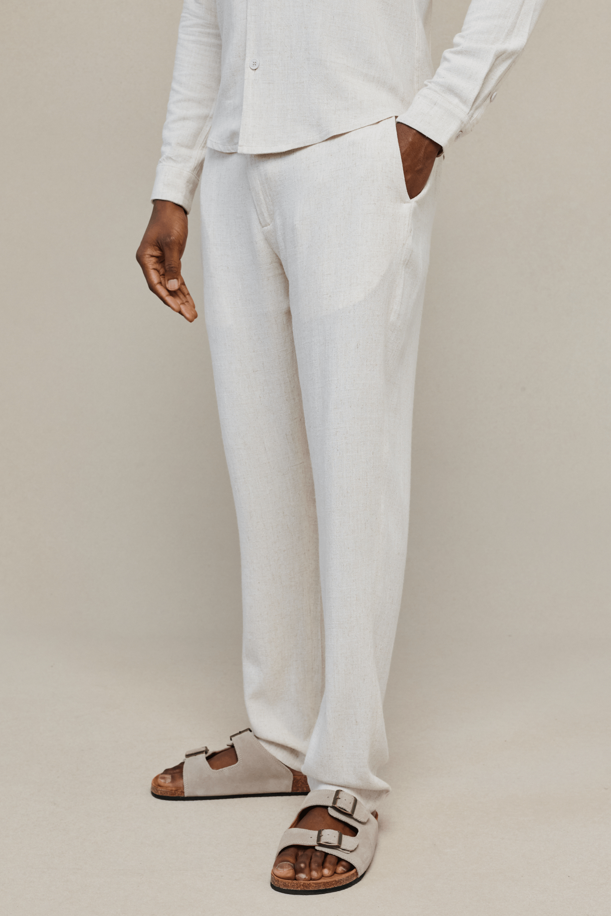 Man wearing an oatmeal cami linen straight leg trousers against a plain background