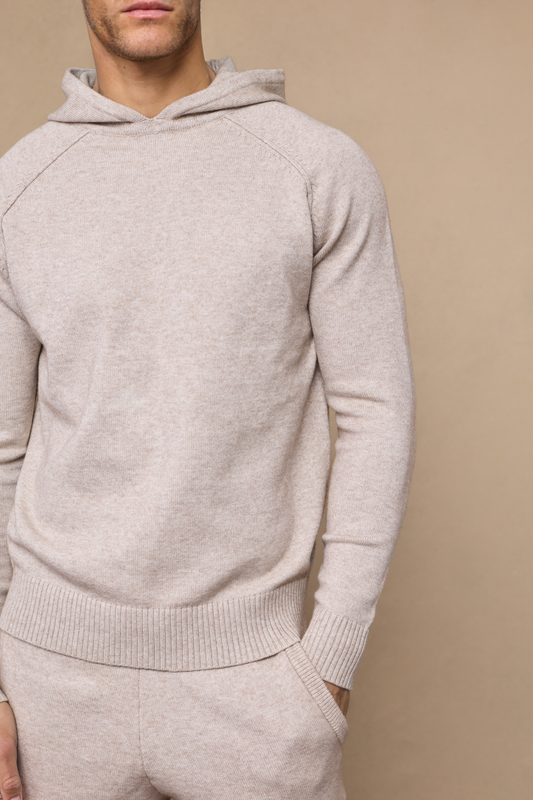 Man wearing an oatmeal rowan knit hoodie against a plain background