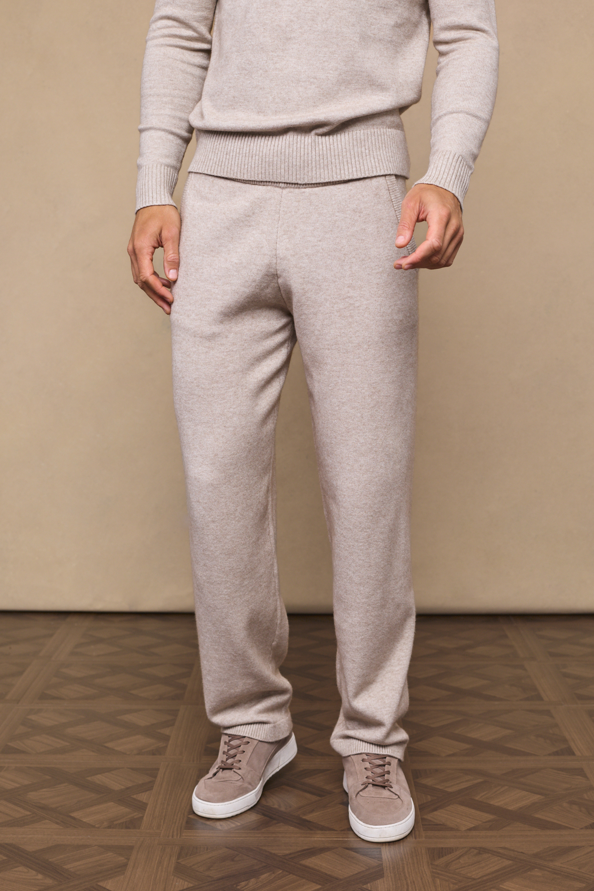Man wearing an oatmeal rowan knit trousers against a plain background