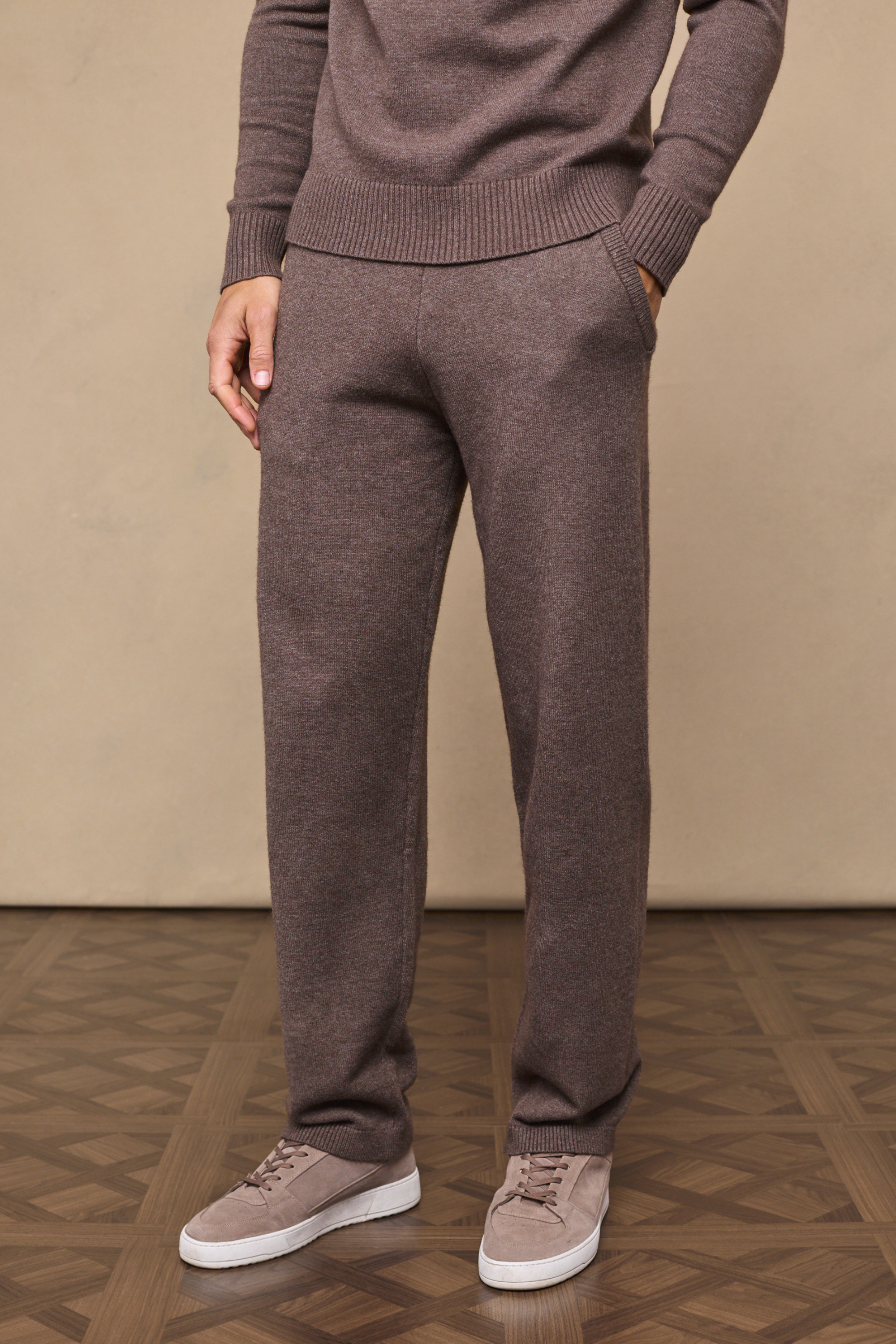 Man wearing a brown marl rowan knit trousers against a plain background