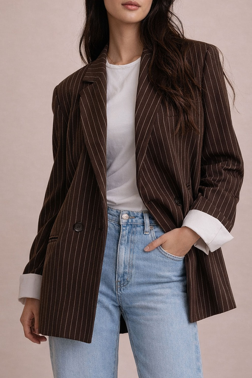 Woman wearing a brown pinstripe blazer over a white shirt and blue jeans on a beige background