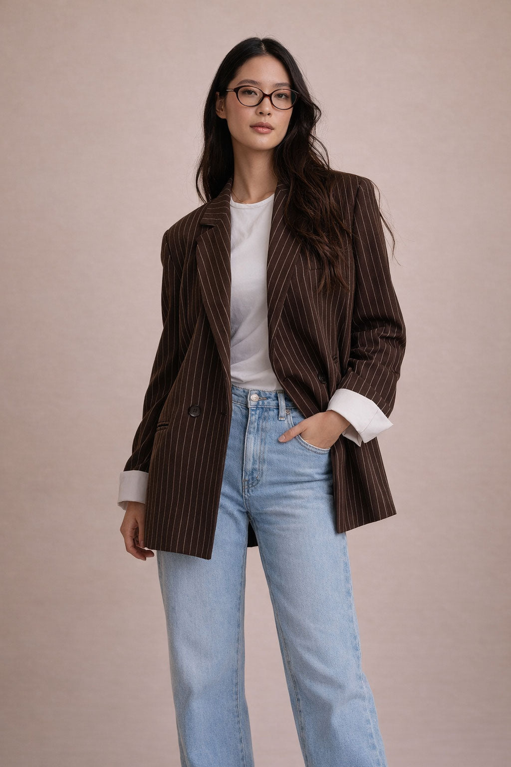Woman wearing a brown pinstripe blazer, white shirt, and light blue jeans against a beige background