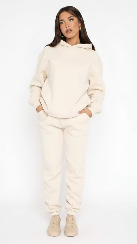 Woman wearing a cream-colored hoodie and pants set with brand logos on a white background
