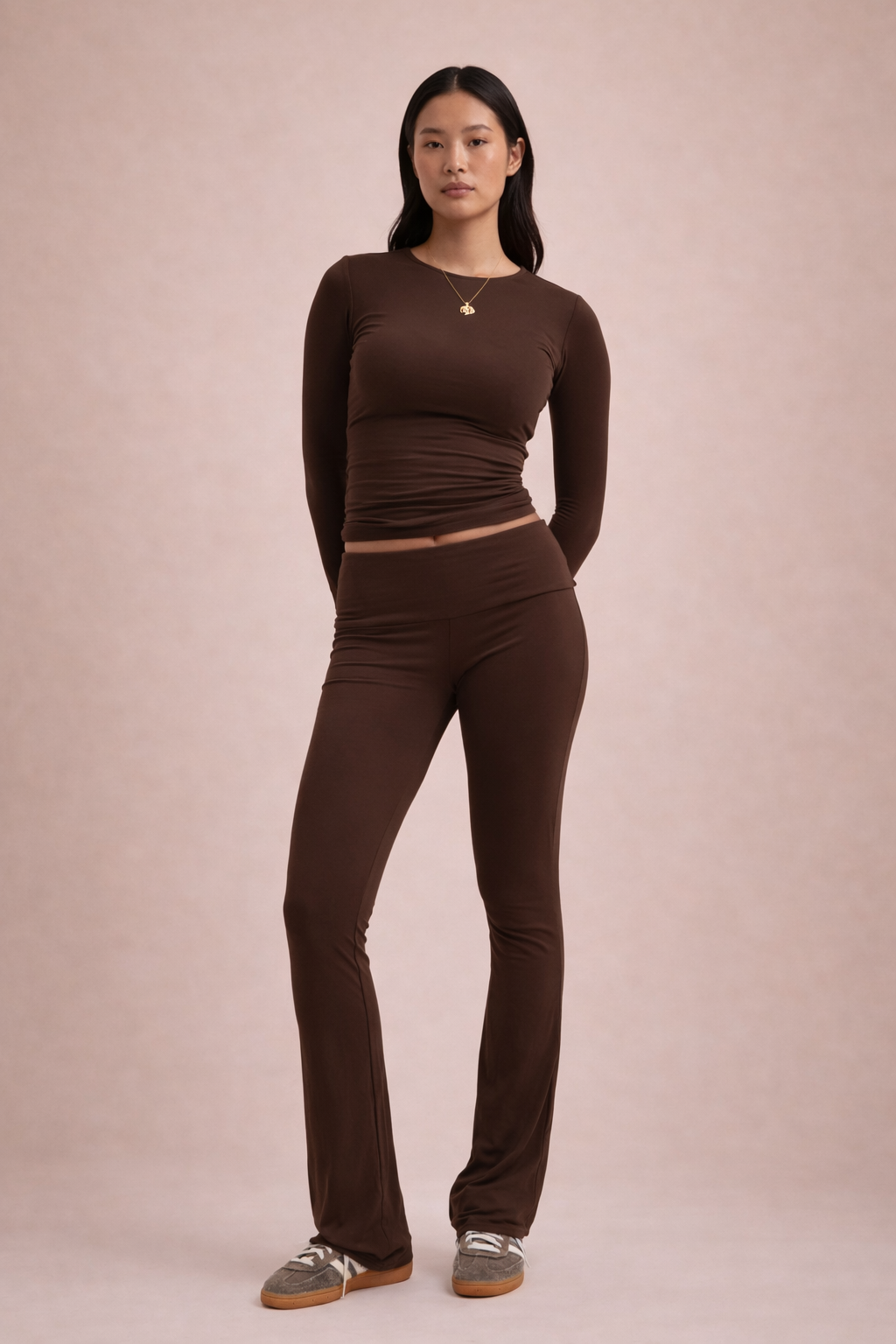 Woman wearing a brown long-sleeve top and pants on a pink background