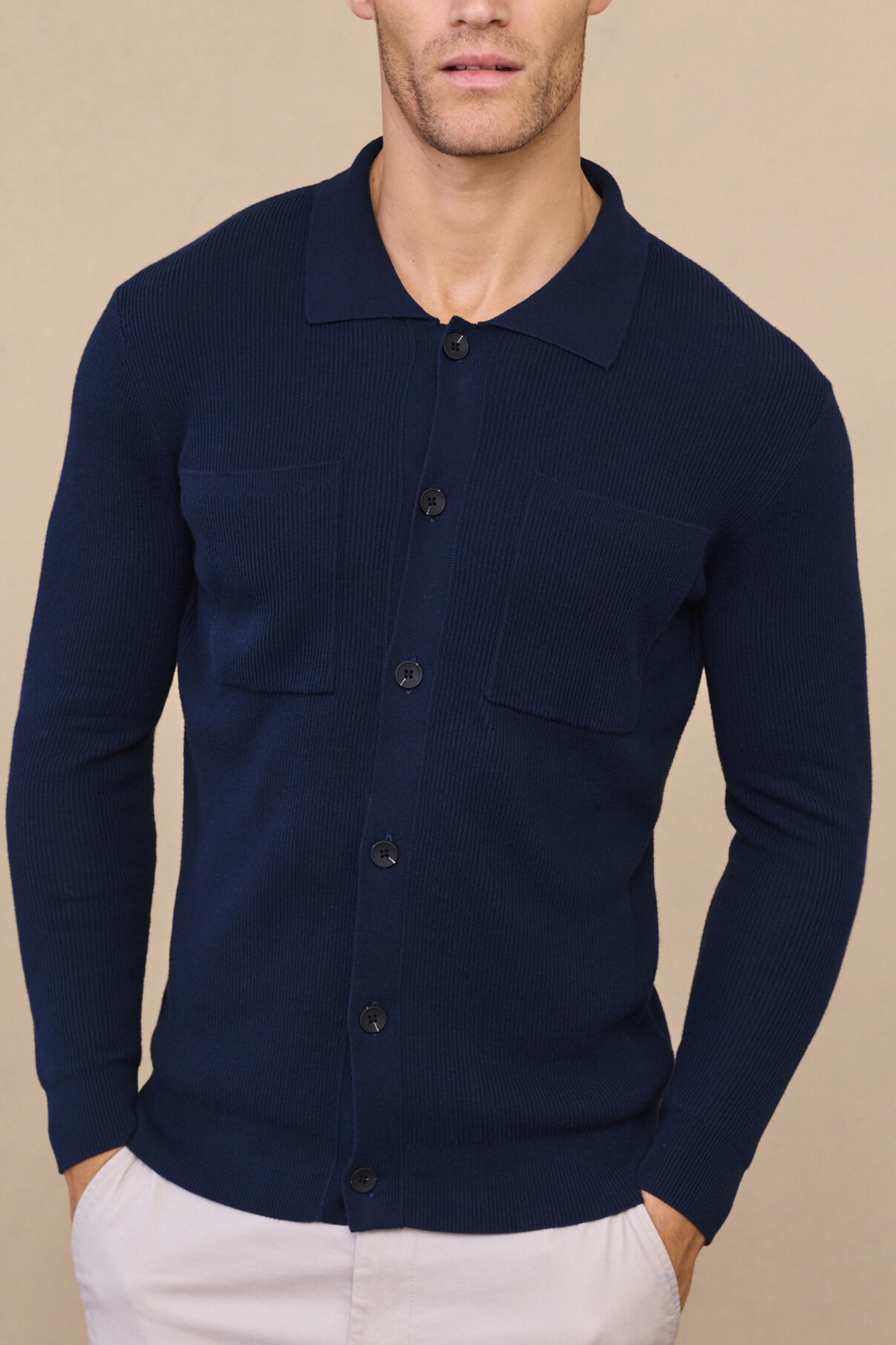 Man wearing a navy elias ribbed pocket cardigan against a soft neutral background